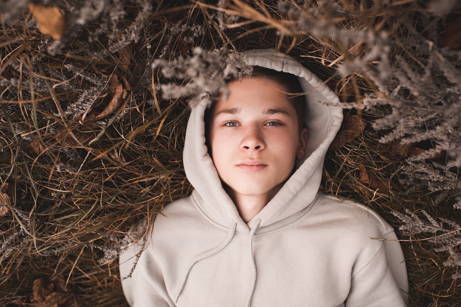 Person in hoodie lying on dried grass.