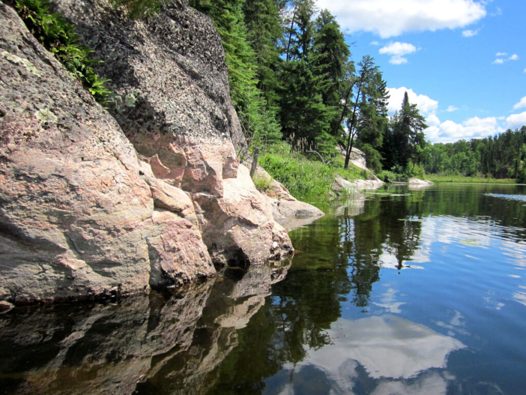 Rocky riverbank with trees reflected in calm water